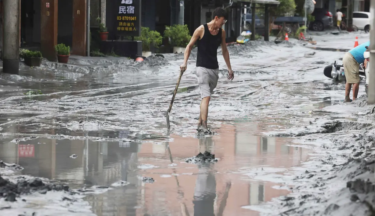 Seorang warga berjalan dengan sekop di sepanjang jalan yang tertutup lumpur di Hualien pada 24 September 2025, setelah bendungan danau jebol akibat terjangan Topan Super Ragasa. (I-Hwa Cheng/AFP)