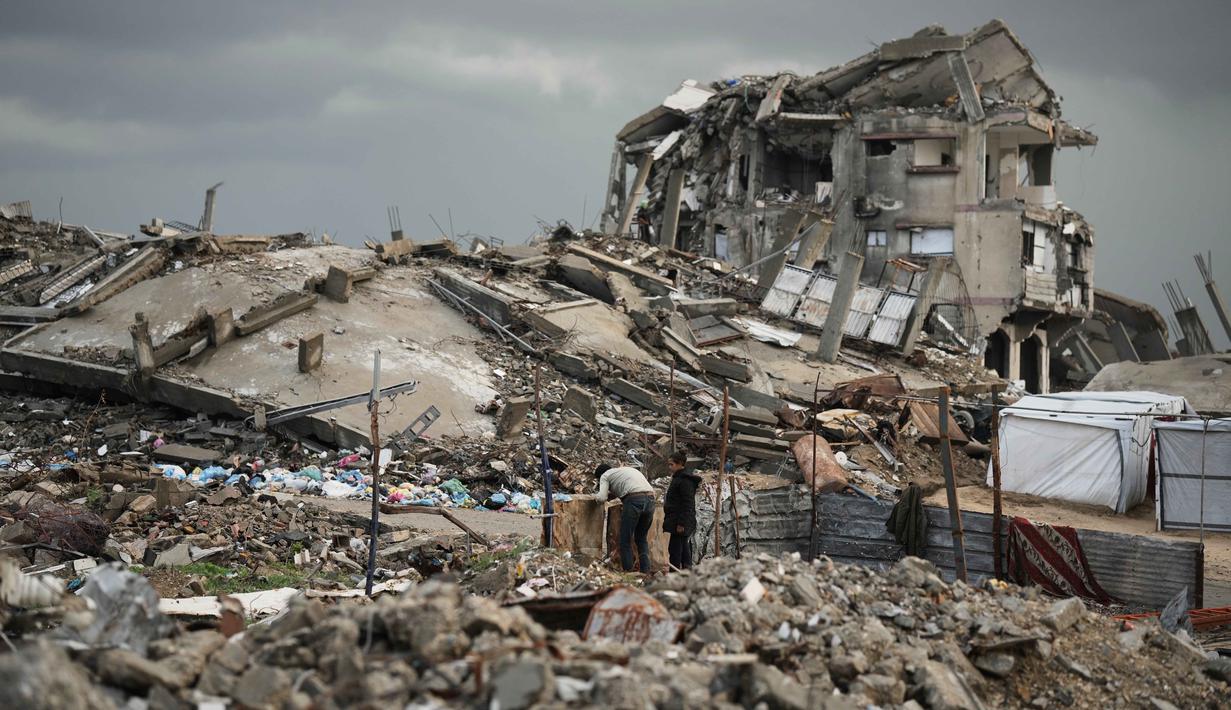 UNRWA menegaskan situasi ini dapat dicegah jika bantuan kemanusiaan tidak terhalang, termasuk dukungan medis dan tempat tinggal layak. Tampak dalam foto, warga Palestina berjalan melewati reruntuhan di tengah cuaca tengah cuaca buruk Kota Gaza, Kamis 11 Desember 2025. (AP Photo/Jehad Alshrafi)