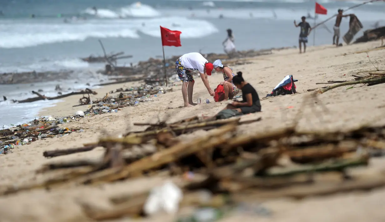 Turis bersantai menikmati Pantai Kuta yang dikelilingi oleh puing-puing dan sampah di Bali, Minggu (9/12). Kawasan pantai Kuta kembali dipenuhi oleh sampah hanyut terbawa oleh gelombang. (SONNY TUMBELAKA / AFP)