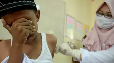 Siswa MIN Ulee Kareng menutup wajah saat mendapat vaksinasi anti virus difteri yang diberikan petugas Kesehatan di Banda Aceh, Aceh, Selasa (20/2). Dari catatan Dinkes, difteri kerap menyerang manusia kisaran usia 4 - 28 tahun. (CHAIDEER MAHYUDDIN/AFP)