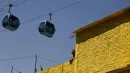 Seorang pria berdiri di atap saat kereta gantung berjalan di antara stasiun Campos Revolucion dan Tlalpexco selama peresmian sistem angkutan umum udara baru yang dijuluki Cablebus di lingkungan Cuautepec, utara Mexico City, Meksiko, Kamis (4/3/2021). (AP Photo/Rebecca Blackwell)