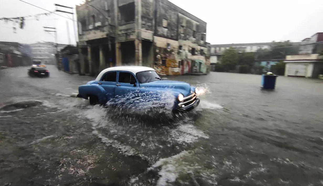 Sebuah mobil tua Amerika Serikat melewati jalan yang banjir di Havana, Kuba, 30 Juni 2021. Hujan deras dan selokan yang tidak berfungsi menyebabkan banjir di jalan-jalan di Havana. (YAMIL LAGE/AFP)