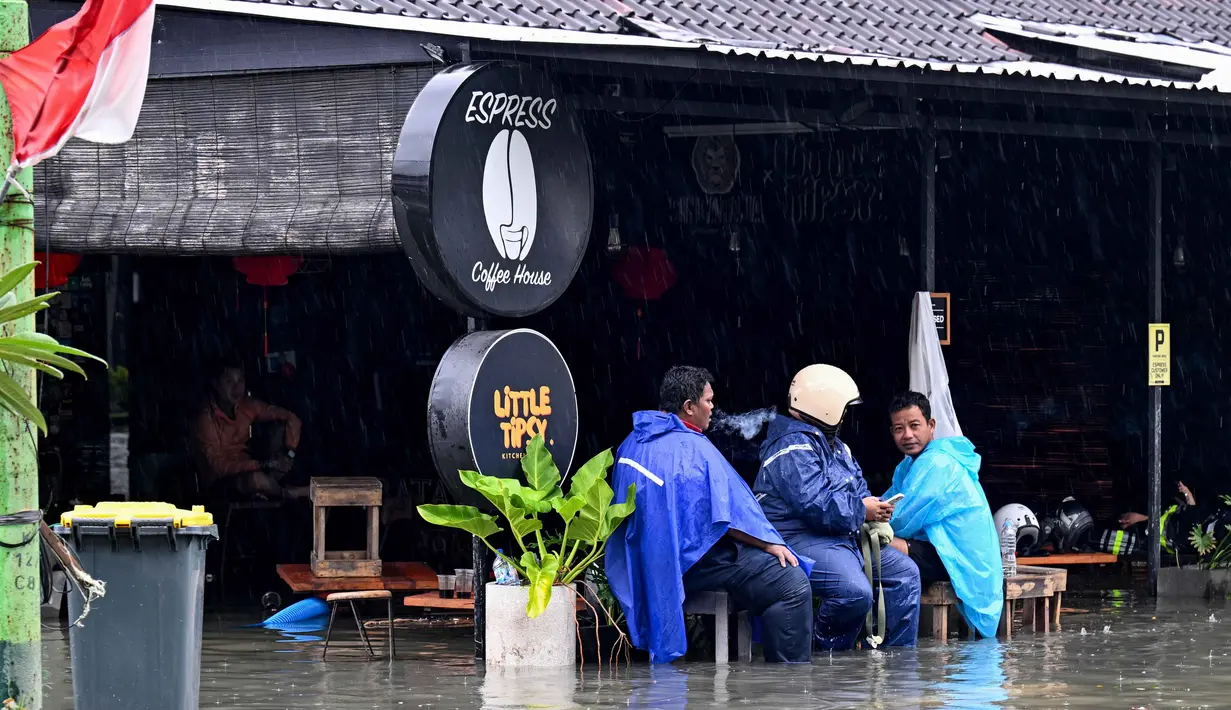 Sebagai upaya penanganan darurat, petugas Badan Penanggulangan Bencana Daerah (BPBD) bersama anggota TNI diterjunkan ke lokasi banjir. Tampak dalam foto, orang-orang duduk di sebuah kafe yang terendam banjir akibat hujan lebat di Legian Kuta, Denpasar, Bali, pada Selasa 24 Februari 2026. (SONNY TUMBELAKA/AFP)