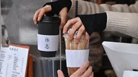 Gambar pada 26 Januari 2023 ini memperlihatkan seorang karyawan membagikan minuman kopi panas dan dingin kepada seorang pelanggan di sebuah kafe di Seoul, Korea Selatan. Budaya kopi bahkan telah melahirkan bahasanya sendiri. Iced Americano dikenal sebagai "Ah-Ah" dan peminum beratnya dikenal sebagai "Eoljuka", kontraksi dari peribahasa baru yang menyatakan  mereka akan mati kedinginan untuk minuman mereka.  (Jung Yeon-je / AFP)