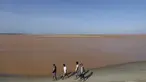 Pengunjung berjalan dipinggir pantai laut Espirito Santo yang airnya berubah menjadi cokelat di Brasil (22/11). Warna air berubah cokelat karena tambang milik Vale SA dan BHP Billiton jebol dan menumpahkan lumpur. (REUTERS/Ricardo Moraes)
