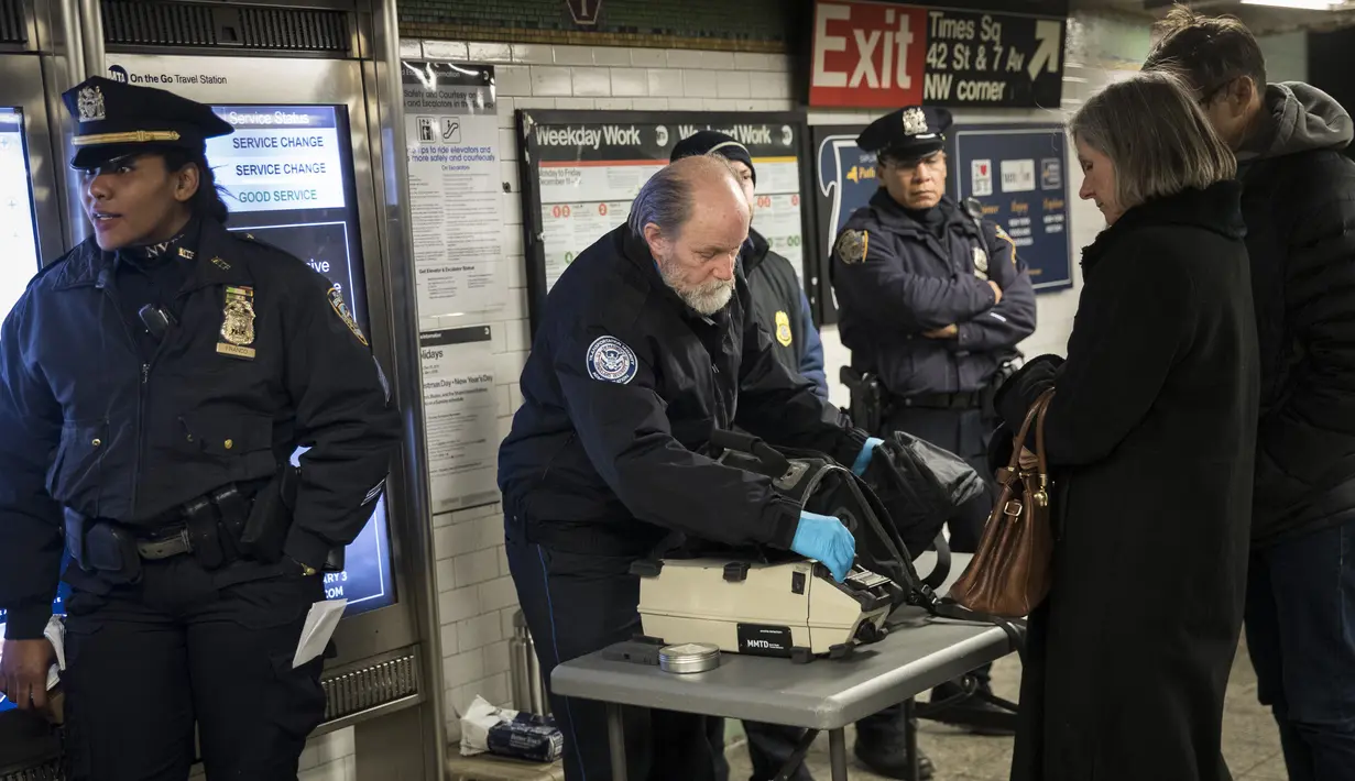 Petugas kepolisian memeriksa tas penumpang saat memasuki stasiun kereta bawah tanah Times Square pada jam sibuk malam di New York City, Senin (11/12). Sebelumnya ledakan bom terjadi di terminal bawah tanah kawasan Manhattan (Drew Angerer/Getty Images/AFP)