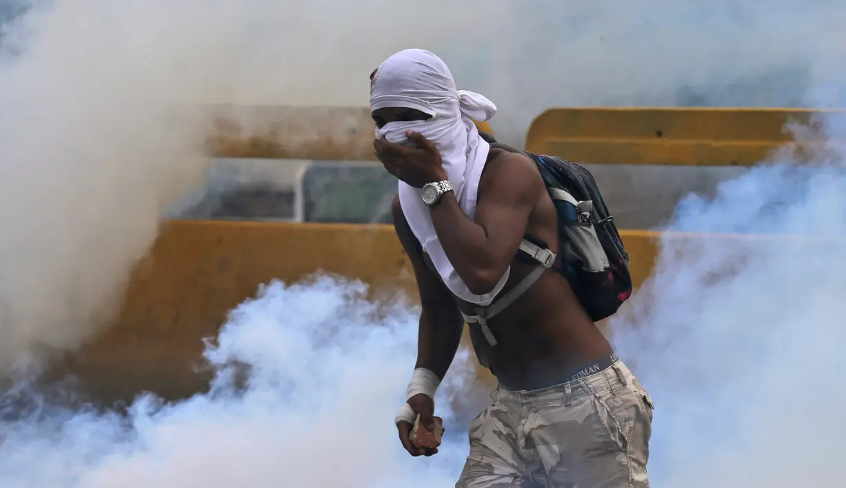 Demonstran menghindari tembakan gas air mata saat bentrokan di Caracas, Venezuela, (6/4). Bentrokan dipicu oleh keputusan kontroversial Mahkamah Agung untuk membubarkan parlemen Venezuela yang mayoritas kelompok oposisi. (AP Photo / Fernando Llano)