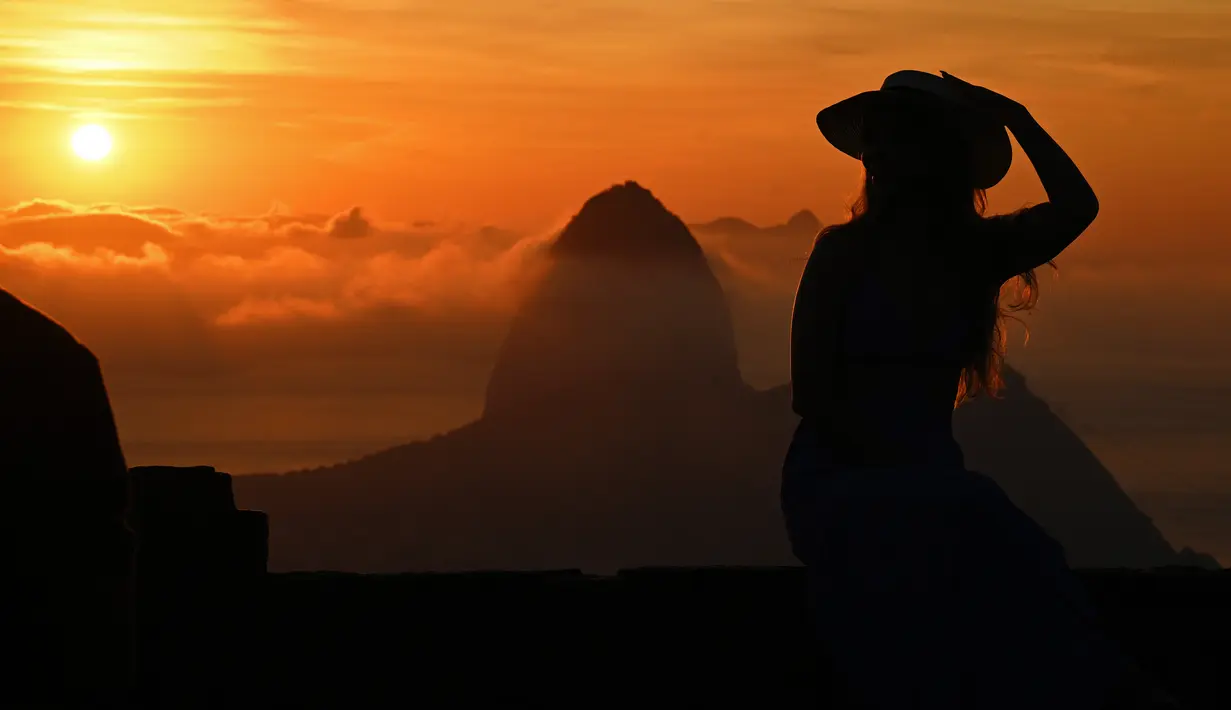 Seorang turis berpose saat matahari terbit dengan latar belakang gunung Sugarloaf di Bukit Corcovado di Rio de Janeiro, Brasil, pada 24 Maret 2023. Lokasi gunung Corcovado yang cukup tinggi juga menarik wisatawan untuk bisa menyaksikan kota Rio de Janeiro dari puncaknya. (Photo by Carl DE SOUZA / AFP)