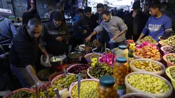 Mereka membeli berbagai kebutuhan pokok dan hidangan tradisional khas Ramadan. Tampak dalam foto, warga Palestina berbelanja acar di pasar Zawiya, Kota Gaza, pada Rabu 18 Februari 2026. (Omar AL-QATTAA/AFP)