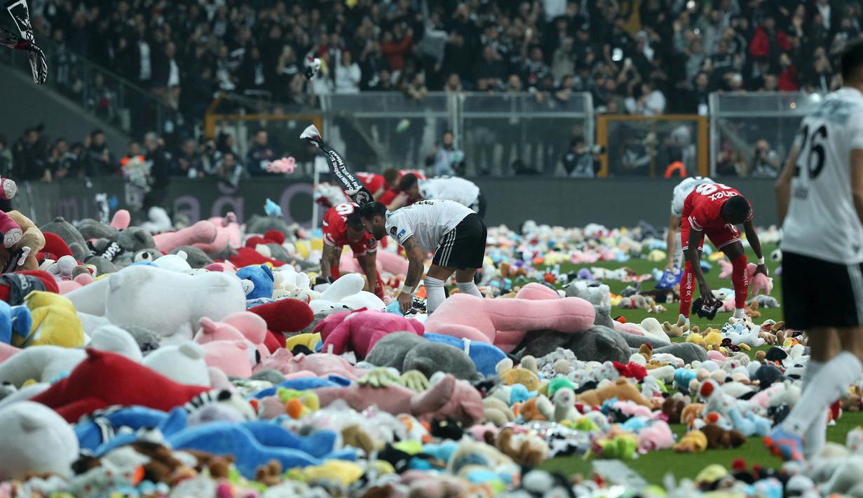 Pemain Besiktas dan Antalyaspor dibantu petugas mengumpulkan boneka yang dilemparkan oleh penonton pada laga lanjutan Liga Turki 2022/2023 yang berlangsung di Stadion Vodafone, Istanbul, Minggu (27/02/2023). Aksi tersebut ditujukan sebagai bentuk sumbangan untuk anak-anak korban gempa Turki. AFP/DHA (DEMIROREN NEWS AGENCY)
