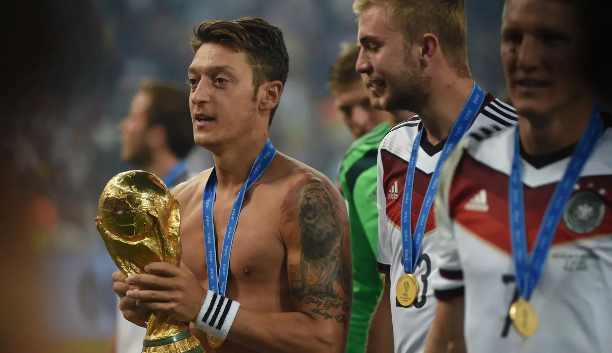 Mesut Oezil. Eks gelandang serang Jerman yang kini masih bermain bersama Istanbul Basaksehir ini tercatat pernah berseragam Arsenal selama 7,5 musim mulai 2013/2014 hingga pertengahan 2020/2021. Seperti Per Mertesacker, ia juga menjadi bagian dalam skuad Tim Panser meraih gelar juara usai mengalahkan Brasil 1-0 lewat perpanjangan waktu di partai final. (AFP/Patrik Stollarz)