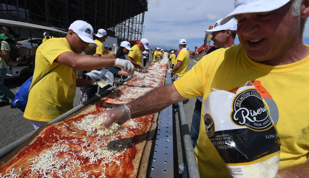 Peserta menaburi keju saat membuat pizza panjang di jalur Auto Club Speedway, di Fontana, California (10/6). Peserta ini membuat pizza untuk memecahkan rekor pizza tepanjang di dunia dengan panjang 1,32 mil atau 2,13 km. (AFP/Mark Ralston)