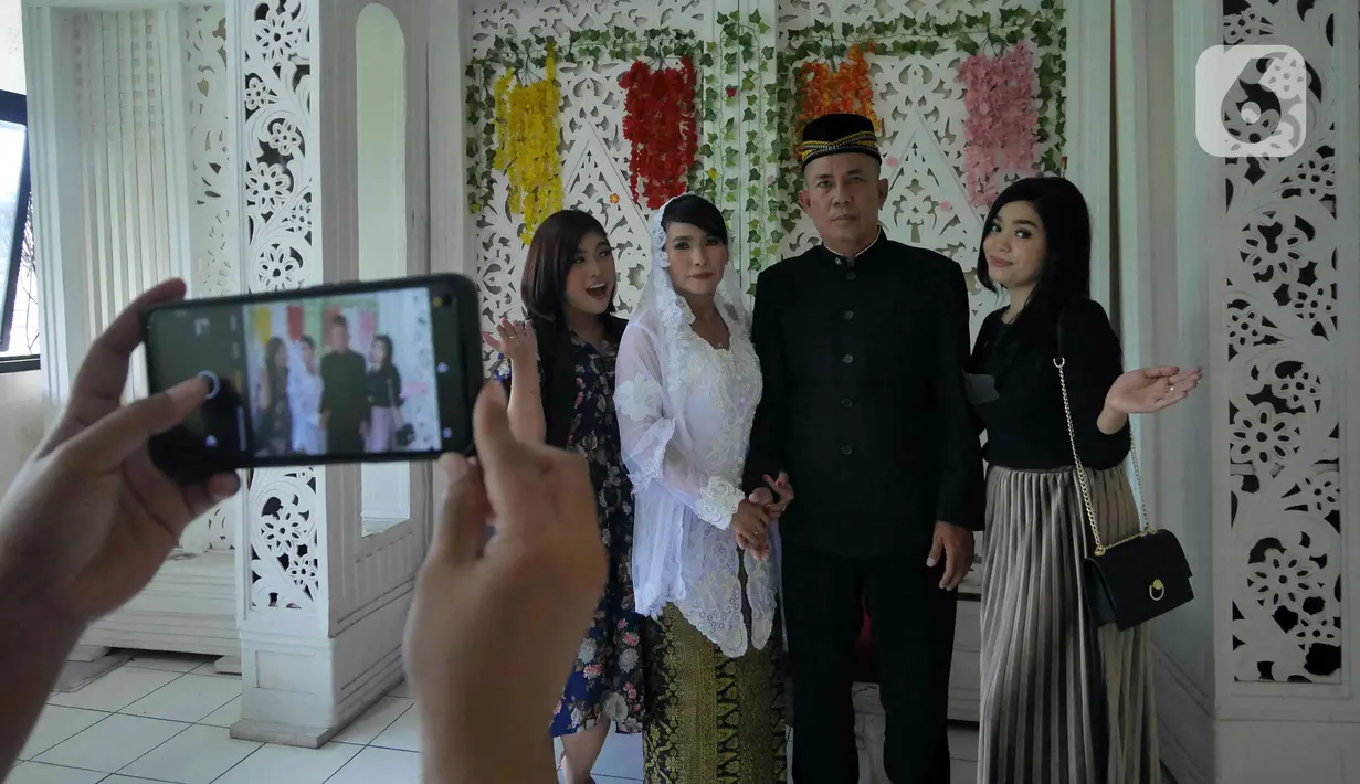 Pasangan Ririn  dan Zaenal berfoto bersama kerabat usai melangsungkan pernikahan di KUA Kecamatan Matraman, Jakarta, Selasa (22/02/2022). Sejumlah pasangan sengaja melangsungkan pernikahan pada hari ini yang memiliki tanggal, bulan, dan tahun unik yakni 22-02-2022. (Liputan6.com/Herman Zakharia)