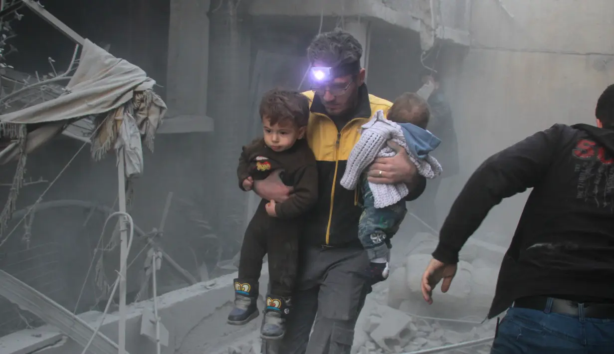 Seorang pria menggendong dua orang anak untuk diselamatkan usai terjadi serangan udara dari pasukan Assad di wilayah Ghouta timur, Suriah (6/2). (AFP Photo/Hamza Al-Ajweh)