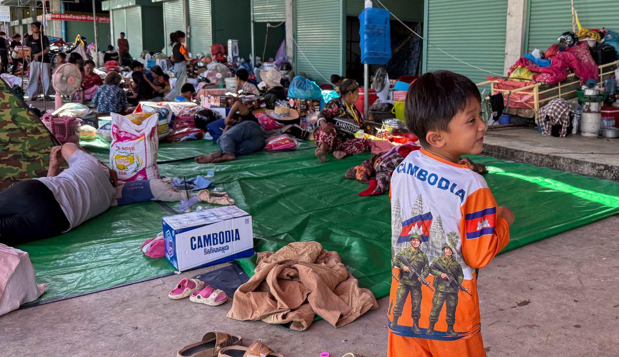 Seorang anak laki-laki mengenakan kaus bergambar tentara berjalan melewati pengungsi lain yang beristirahat di kamp sementara di provinsi Banteay Meanchey pada Sabtu 13 Desember 2025, di tengah bentrokan di sepanjang perbatasan Kamboja-Thailand. Ketegangan di perbatasan Kamboja-Thailand kembali mencapai titik kritis. (Suy Se/AFP)