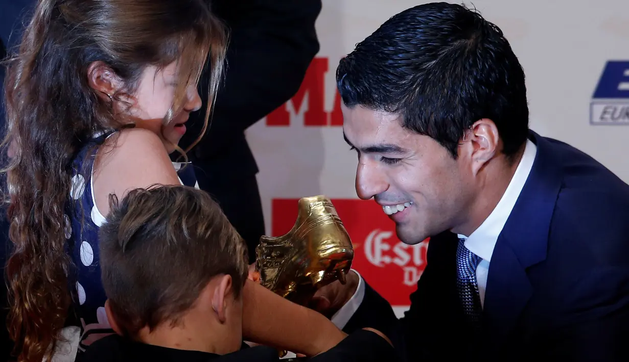 Penyerang Barcelona, Luis Suarez menunjukan sepatu emas 2016 kepada kedua anaknya di Barcelona, Spanyol (20/10). Suarez mengalahkan rivalnya, seperti Gonzalo Higuain, Cristiano Ronaldo, dan Zlatan Ibrahimovic. (REUTERS/Albert Gea)