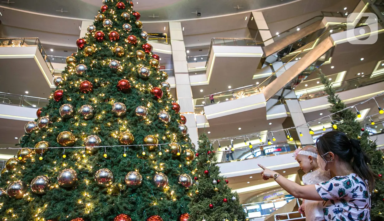 Pengunjung melihat Pohon Natal Raksasa  di Mall Taman Anggrek, Jakarta, Senin (21/12/2020). Mengangkat tema “Christmas Merry and Bright”,  dalam kondisi pandemi Covid-19, Mal Taman Anggrek tetap mendekor interior mal. (Liputan6.com/Faizal Fanani)