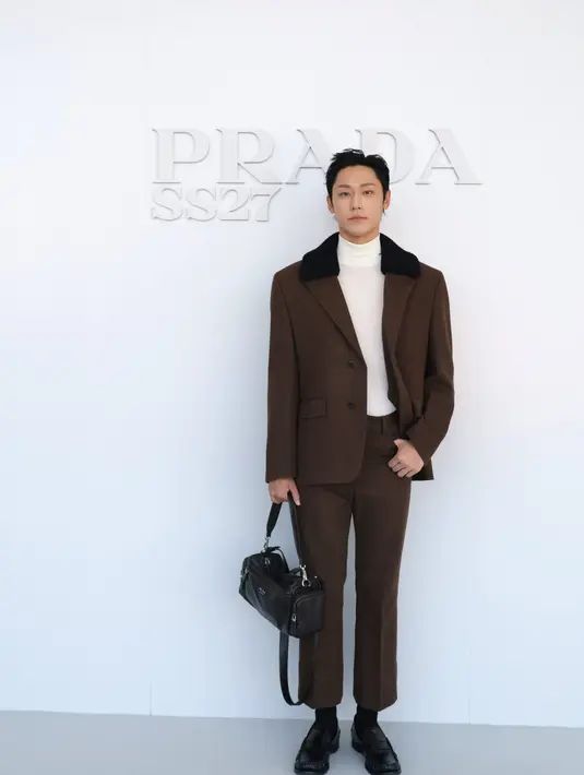 Lee Do-Hyun tampil dengan setelan jas cokelat berkerah bulu domba hitam, dipadukan turtleneck krem dan tas kulit hitam. [dok. Prada]