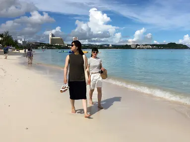 Pengunjung berjalan menyusuri tepi pantai Tumon di Guam, Kamis (10/8). Meskipun suasana ketegangan di kawasan itu meningkat  terkait ancaman bom nuklir Korea Utara, warga Guam tetap beraktivitas seperti biasa. (AP Photo/Tassanee Vejpongsa)