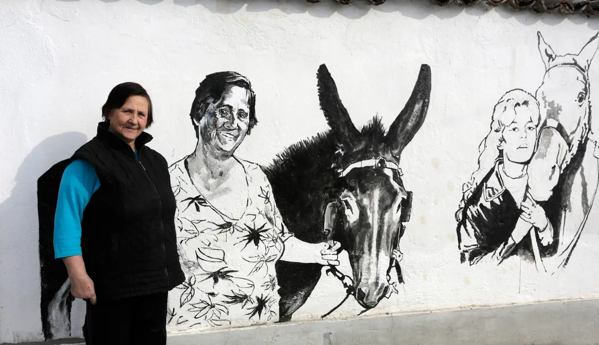 Sabka (82) melintasi dinding yang dilukis mural bergambar Putri Diana, di desa Staro Zhelezare, Bulgaria, Kamis (27/7). Penduduk setempat memenuhi dinding bagian luar rumah mereka dengan mural sejumlah tokoh dan musisi dunia. (AP Photo/Valentina Petrova)
