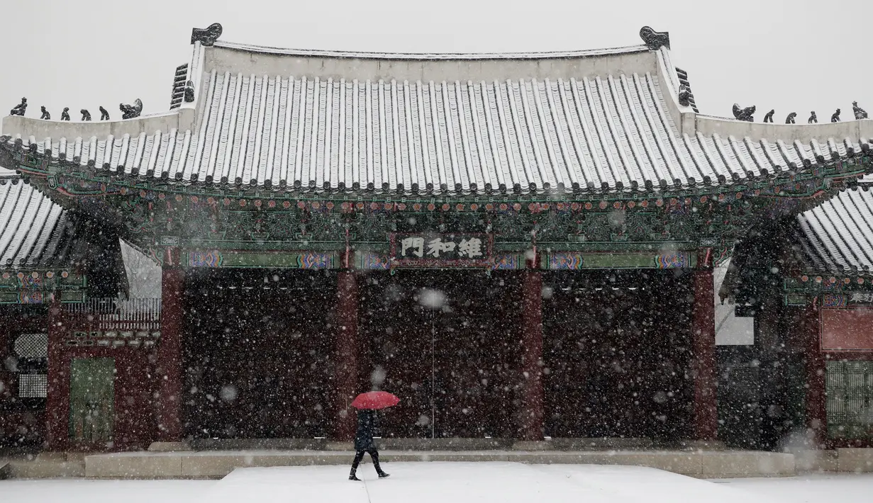 Seorang wanita menggunakan payung  berjalan saat hujan salju di Istana Gyeongbok di Seoul, Korea Selatan (13/12). Istana Gyeongbok merupakan kerajaan utama selama Dinasti Joseon dan salah satu landmark terkenal di kota tersebut. (AFP Photo/Lee Jin-man)