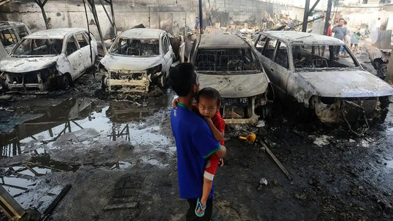 Seorang pria sambil menggendong anak melihat kondisi mobil yang hangus akibat kebakaran Depo Pertamina Plumpang (merdeka.com/Arie Basuki)