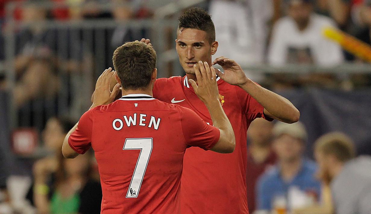<p>Striker Manchester United, Michael Owen (belakang) merayakan gol yang dicetak Federico Macheda ke gawang New England Revolution pada laga pramusim 2011/2012 di Gillette Stadium, Foxboro (13/7/2011). Michael Owen langsung mengenakan nomor punggung 7 saat pertama kali didatangkan MU dari Liverpool hingga meninggalkan MU pada akhir musim 2011/2012. Ia mewarisi nomor keramat tersebut secara berurutan dari Andrey Kanchelskis, David Beckham hingga Cristiano Ronaldo. (AFP via Getty Images/Jim Rogash)</p>