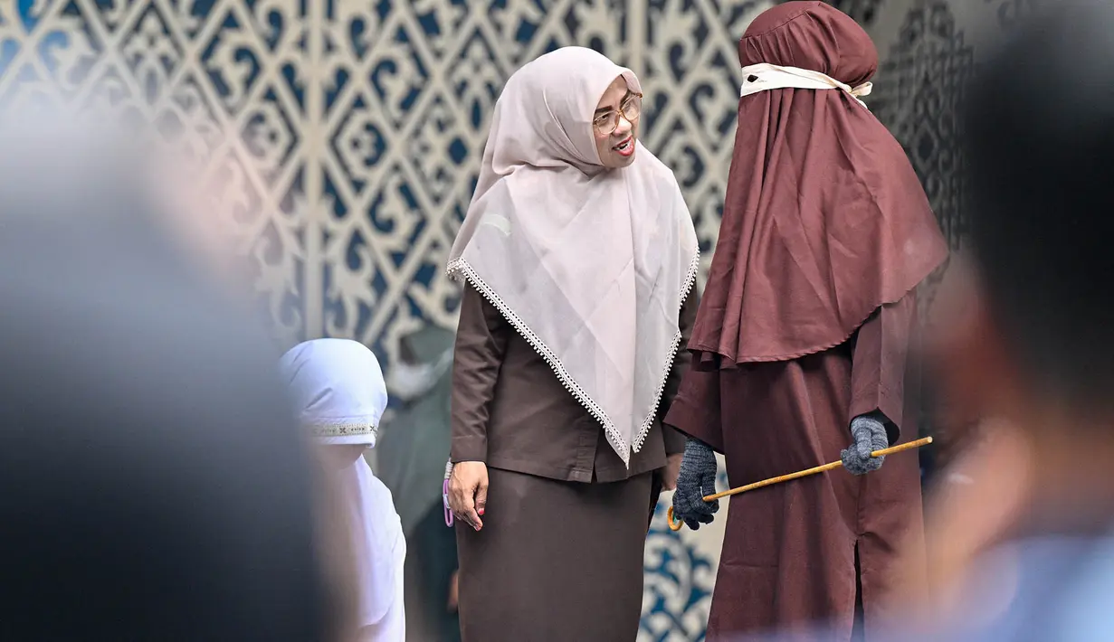 Seorang petugas penegak hukum berbicara dengan petugas syariat saat seorang perempuan sedang menjalani hukuman cambuk di Banda Aceh,  Kamis, 20 Agustus 2026. (AFP/ Chaideer Mahyuddin)