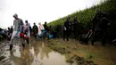 Penonton Festival Glastonbury melewati jalanan yang banjir dan berlumpur saat tiba di Worthy Farm, Somerset, Inggris, (22/6). Glastonbury Festival 2016 dimulai 22 Juni-26 Juni dengan penonton berjumlah ratusan ribu orang. (REUTERS / Stoyan  Nenov)