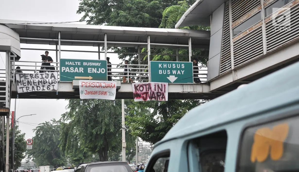 Warga melintasi spanduk dukungan Persija yang terpasang di JPO, Jakarta, Minggu (9/12).  Dalam spanduk tersebut bertuliskan berbagai ungkapan dukungan dan doa para The Jakmania agar Persija menjadi juara Liga 1 2018. (Merdeka.com/Iqbal S. Nugroho)