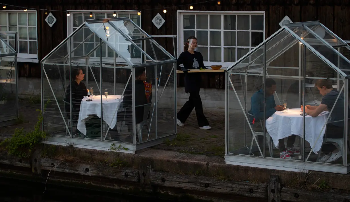 Staf menggunakan papan panjang untuk menyajikan makanan kepada pelanggan dalam kabin kaca "quarantine greenhouses" selama uji coba, ketika Belanda berjuang melawan penyebaran COVID-19, di restoran Mediamatic, Amsterdam pada 5 Mei 2020. (AP/Peter Dejong)