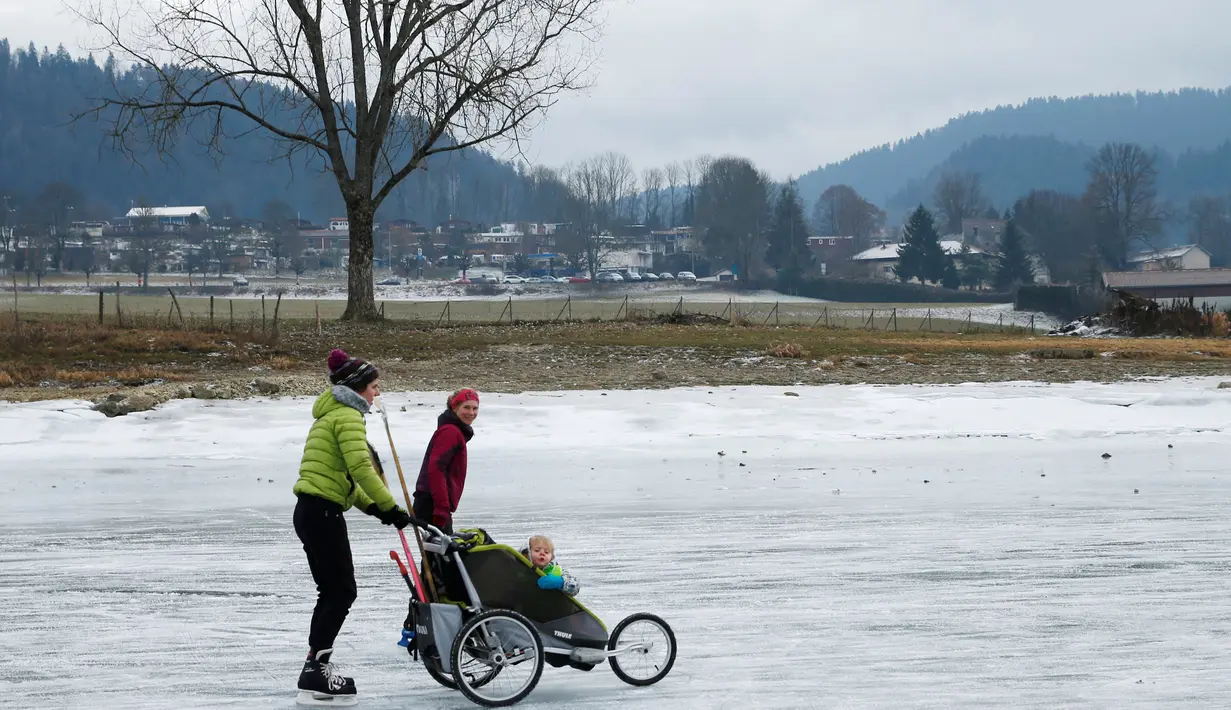 Seorang wanita membawa bayinya bermain ice skating atau seluncur es di atas sungai Doubs yang membeku di perbatasan Perancis Les Brenets, Swiss, Senin (2/1). Sungai ini menjadi objek wisata es yang diminati warga. (REUTERS/Denis Balibouse)