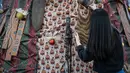 Instalasi dekorasi Pohon Natal ini berdiri setinggi tujuh meter dengan diameter 3,3 meter dan dibuat dari rangka kayu serta kain bermotif khas Papua. Tampak dalam foto, salah satu mahasiswa memasang sentuhan akhir pada instalasi dekorasi berbentuk pohon Natal dengan motif budaya Papua di Perpustakaan Petra Christian University (PCU), Surabaya, Jawa Timur, Kamis 18 Desember 2025. (JUNI KRISWANTO/AFP)