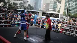 Dua petinju saling melepaskan pukulan pada pertandingan tinju amatir saat Car Free Day di kawasan Bundaran HI, Jakarta, Minggu (29/4). Pertandingan tanpa pemenang ini digelar Persatuan Tinju Amatir Indonesia (Pertina). (Liputan6.com/Faizal Fanani)