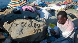 Seorang imigran membaca Al-Quran saat bulan suci ramadan di atas bebatuan laut Ventimiglia, perbatasan antara Italia-Prancis, (18/6/2015). Sekitar 200 imigran berada di bebatuan pantai untuk melintasi perbatasan Italia. (REUTERS/Eric Gaillard)