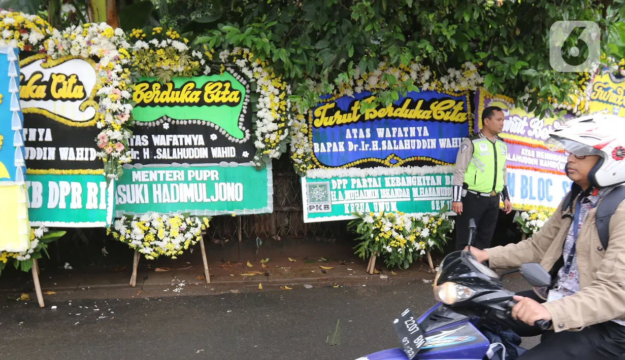 Polisi berdiri dekat karangan bunga ucapan duka cita atas meninggalnya KH Salahuddin Wahid atau Gus Sholah di kawasan Mampang Prapatan, Jakarta, Senin (3/2/2020). Gus Sholah meninggal usai perawatan pascaoperasi jantung di Rumah Sakit Jantung Harapan Kita, Jakarta. (Liputan6.com/Herman Zakharia)