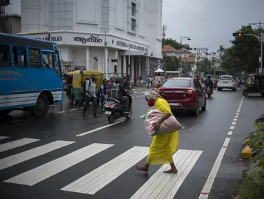 Seorang wanita tua yang mengenakan masker berjalan tanpa alas kaki melalui zebra cross di Kochi, negara bagian Kerala, India, Rabu (6/7/2022). Negara bagian selatan itu telah mewajibkan penggunaan masker di tempat-tempat umum menyusul meningkatnya kasus COVID-19. (AP Photo/ RS Iyer)