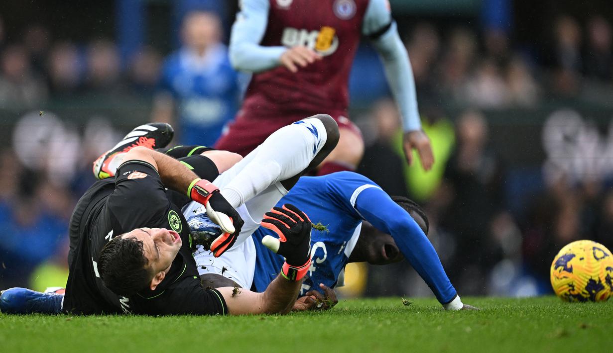 Reaksi kesakitan kiper Aston Villa, Emiliano Martinez (kiri) saat bertabrakan dengan pemain Everton, Amadou Onana pada laga lanjutan Liga Inggris 2023/2024 di Goodison Park, Liverpool, Inggris, Minggu (14/01/2024) malam WIB. (AFP/Paul Ellis)