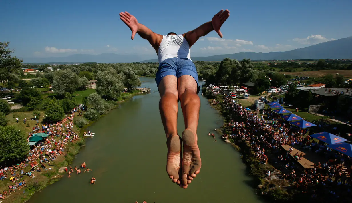 Penonton menyaksikan dari tepi sungai saat seorang peserta melakukan terjun bebas dari jembatan Ura e Shejnt dalam kompetisi menyelam tradisional ke-68 di Gjakova, Kosovo, 22 Juli 2018. Kompetisi ini dilakukan dari ketinggian 22 meter. (AP/Visar Kryeziu)