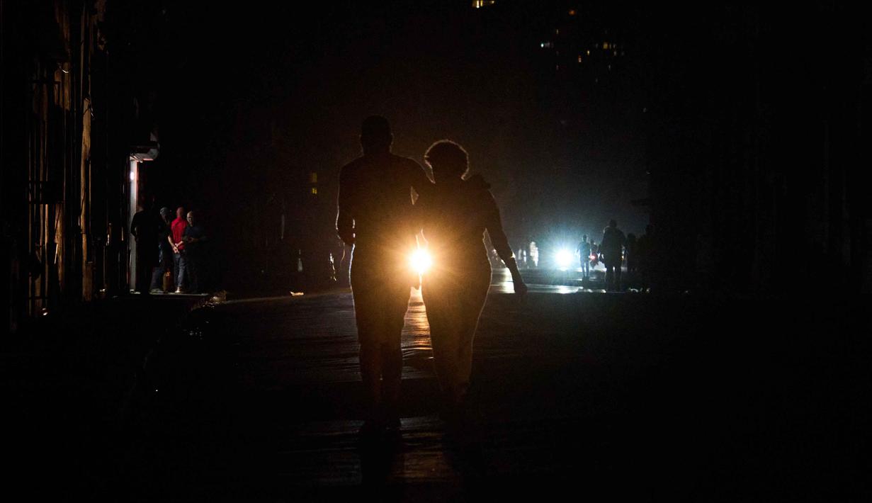 Infrastruktur pembangkit yang menua serta kekurangan bahan bakar membuat pemadaman listrik berkepanjangan, bahkan bisa berlangsung hingga 20 jam setiap hari, menjadi hal biasa di sejumlah wilayah. Tampak dalam foto, orang-orang menyeberang jalan saat pemadaman listrik di Havana, Kuba, Rabu 4 Maret 2026. (AP Photo/Ramon Espinosa)