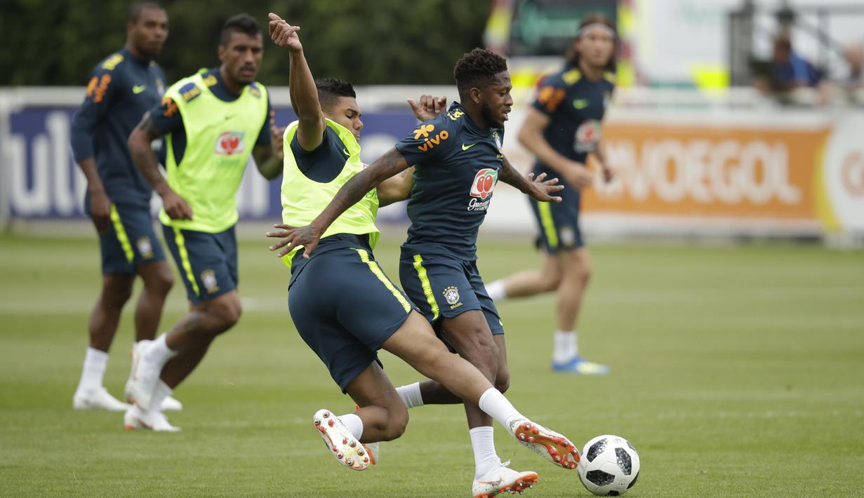 Fred (kanan) saat di jegal rekannya Casemiro pada sesi latihan di lapangan latihan Tottenham Hotspur football club, Inggris, (7/6/2018). Fred mengalami masalah di engkel kaki. (AP/Matt Dunham)