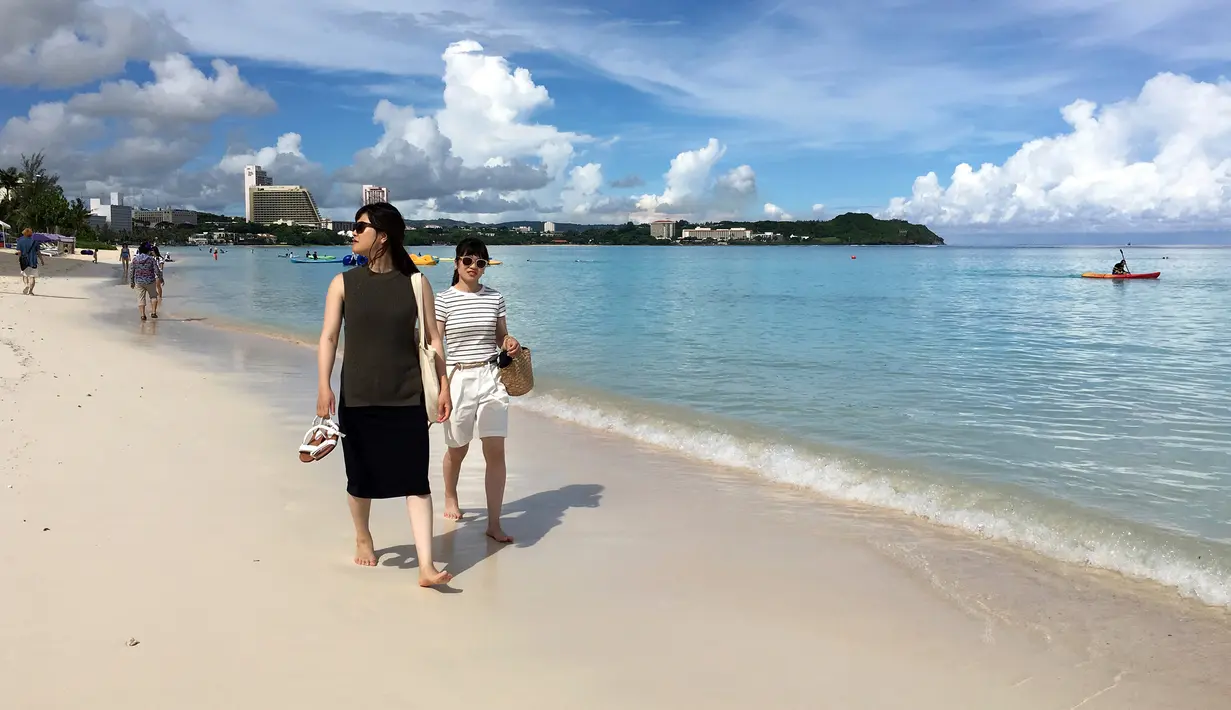 Pengunjung berjalan menyusuri tepi pantai Tumon di Guam, Kamis (10/8). Meskipun suasana ketegangan di kawasan itu meningkat  terkait ancaman bom nuklir Korea Utara, warga Guam tetap beraktivitas seperti biasa. (AP Photo/Tassanee Vejpongsa)