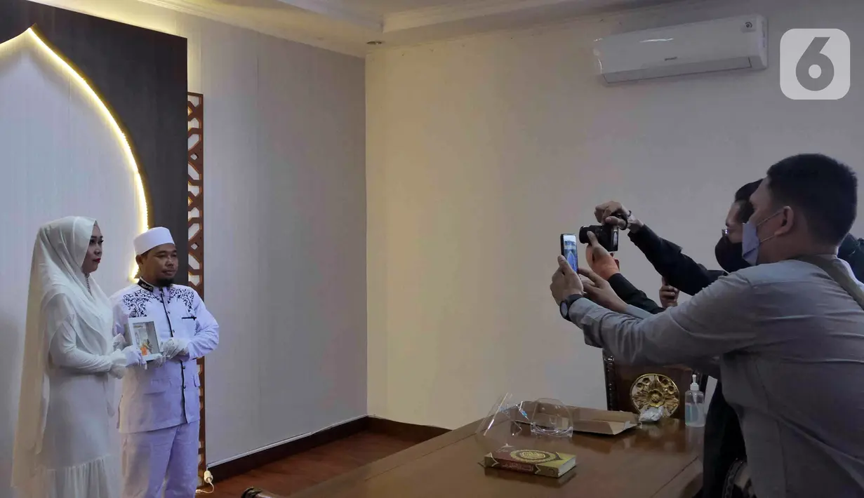 Pasangan Dewi dan Dinar foto bersama saat melangsungkan pernikahan di KUA Kecamatan Meteng, Jakarta, Selasa (22/02/2022). Sejumlah pasangan sengaja melangsungkan pernikahan pada hari ini yang memiliki tanggal, bulan, dan tahun unik yakni 22-02-2022. (Liputan6.com/Herman Zakharia)