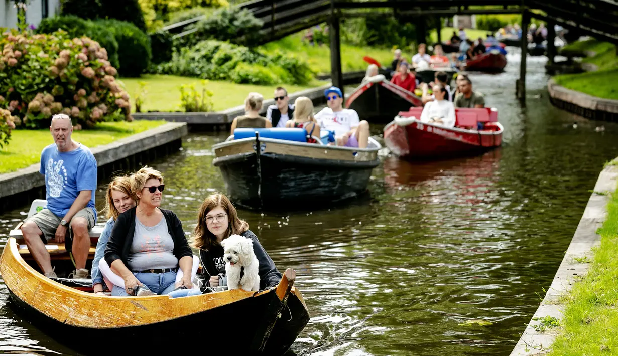 Turis bersama anjingnya menaiki perahu menyusuri sungai di Giethoorn yang menjadi tujuan wisata favorit di Belanda, 6 Agustus 2019. Mendapat julukan 'Venice of the North', kota tersebut menggunakan kanal-kanal sebagai jalan dan lalu lalang transportasi sehari-hari. (Robin van Lonkhuijsen/ANP/AFP)