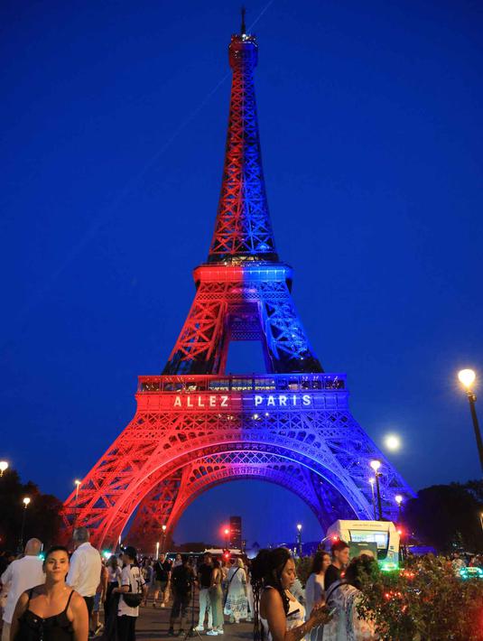 Orang-orang berjalan di bawah Menara Eiffel yang diterangi cahaya warna-warna khas, dengan pesan bertuliskan "Allez Paris" ("Ayo, Paris"), pada malam menjelang pertandingan final Liga Champions 2025/2026 antara Paris Saint-Germain (PSG) dan Arsenal, Kamis 29 Mei 2026. (Ludovic MARIN/AFP)