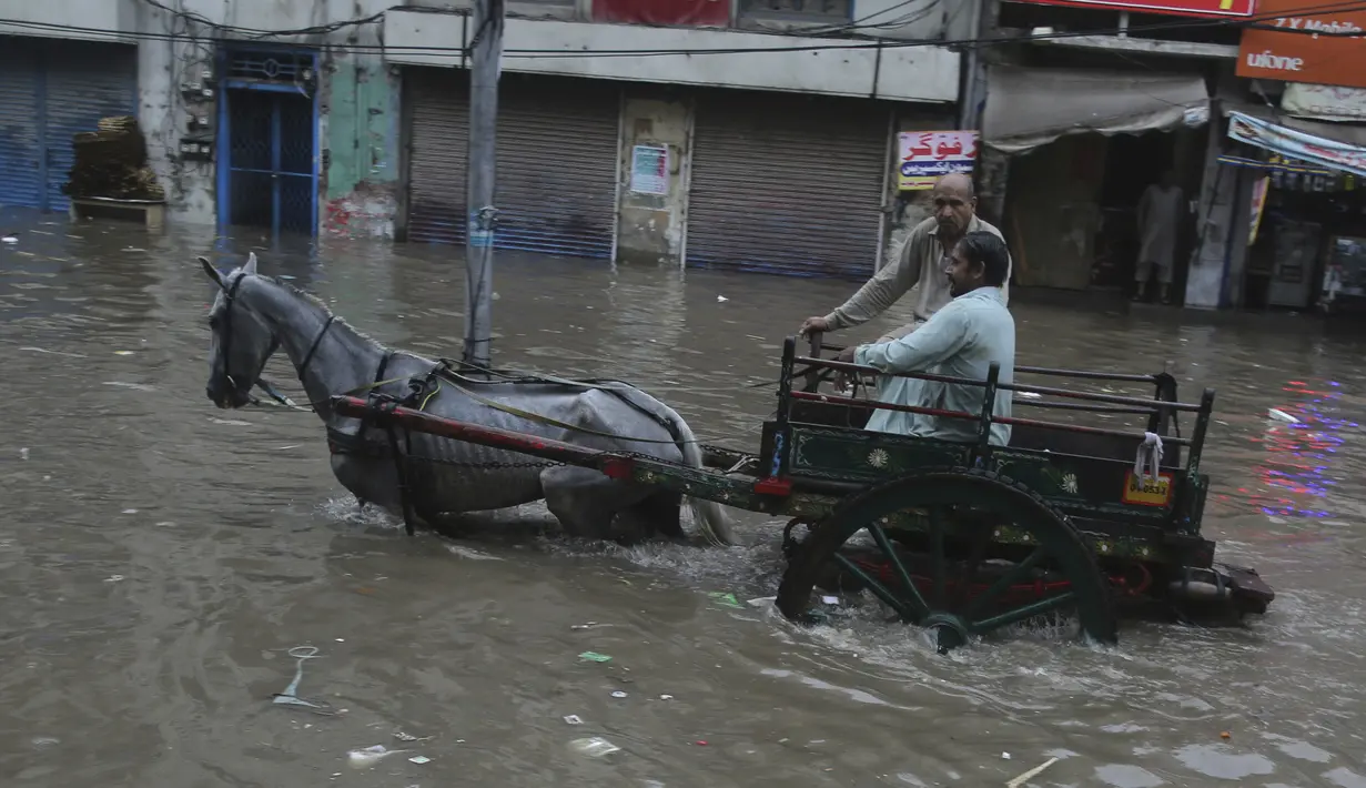 Seorang pria membawa kuda menyeberangi jalan yang banjir setelah hujan deras di Lahore, Pakistan (16/7/2019). Di Kashmir yang dikelola Pakistan, para pejabat pemerintah mengatakan sedikitnya 23 orang tewas setelah hujan lebat memicu banjir bandang. (AP Photo/K.M. Chaudary)