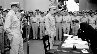 Jenderal AS Douglas MacArthur (kiri) menyaksikan Menteri Luar Negeri Jepang Manoru Shigemitsu menandatangani dokumen penyerahan di atas kapal perang USS Missouri, Teluk Tokyo, 2 September 1945. Penandatanganan ini menandai berakhirnya Perang Dunia II. (AP Photo/C.P. Gorry, File)