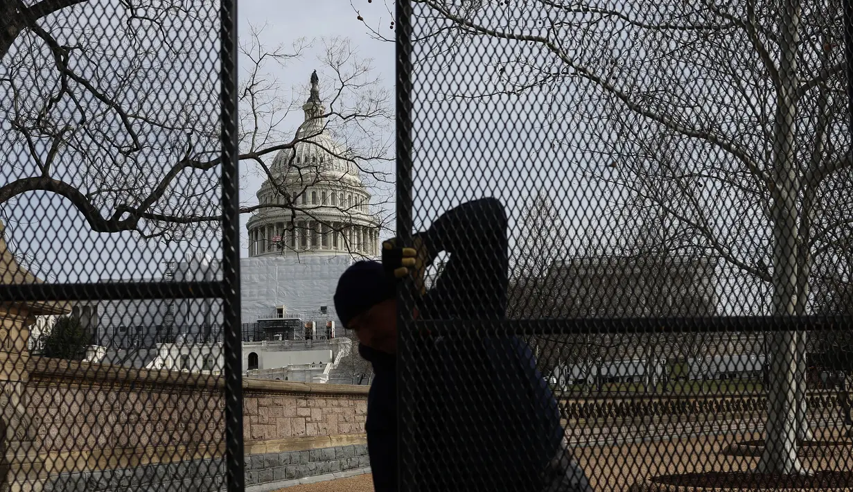 Seorang pekerja membantu memasang pagar keamanan di sekitar U.S. Capitol di Washington, DC pada Minggu (5/2/2023). Pagar sedang dipasang sebagai bagian dari langkah-langkah keamanan yang ditingkatkan menjelang pidato kenegaraan Presiden Joe Biden pada hari Selasa. (Kevin Dietsch/Getty Images/AFP)