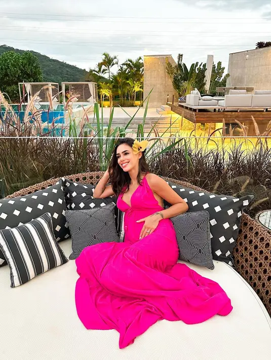 Pesona cantik bumil ini kian terpancar saat dibalut strap dress berwarna fuschia dan bunga yang disematkan di telinganya. [Foto: IG/brunabiancardi].