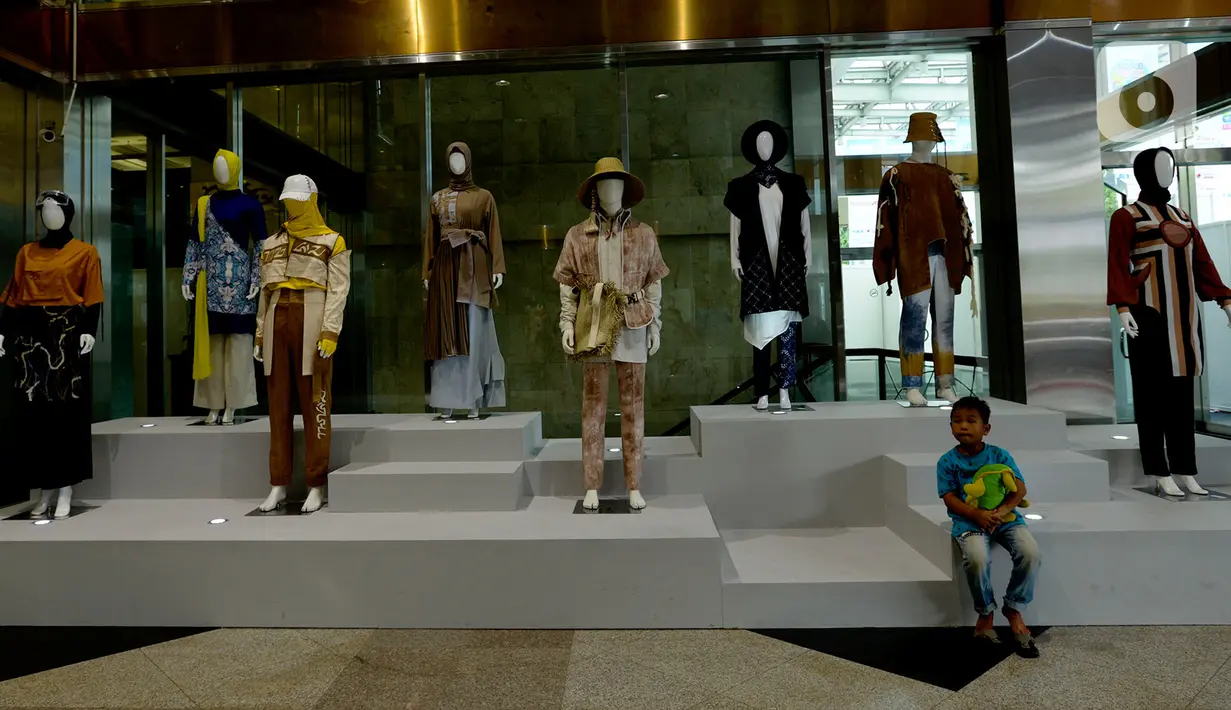 Seorang anak duduk dekat deretan pakaian dalam Muslim Fashion Festival (Muffest) 2020 di Jakarta Convention Center (JCC), Jakarta, Kamis (20/2/2020). Muffest 2020 ajang pameran para pelaku industri busana muslim Tanah Air. (merdeka.com/Imam Buhori)